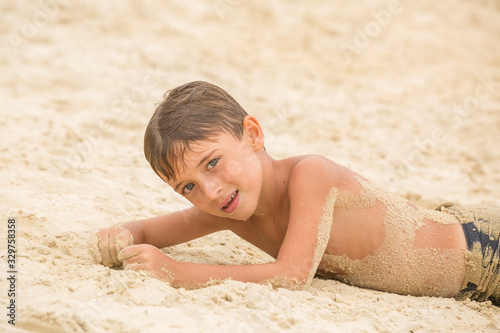 Kid boy with body in send lying on a sandy beach