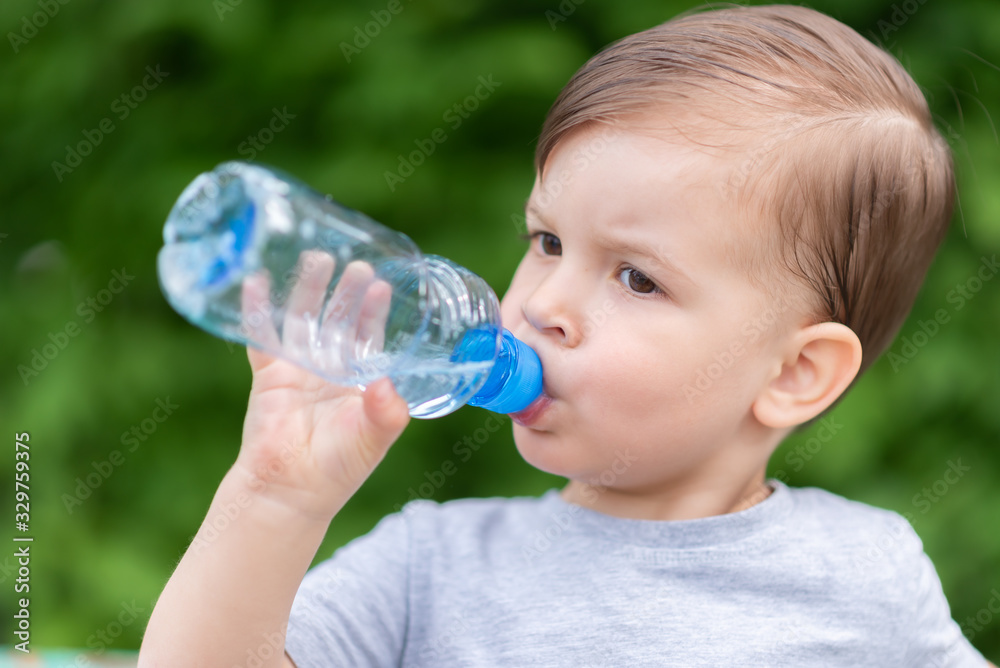 handsome boy drinks clear water from a bottle on a sunny day outside handsome boy drinks clear water from a bottle on a sunny day outside