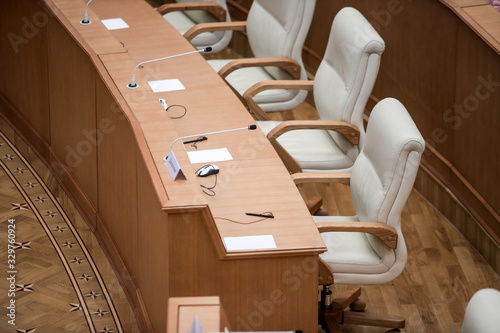 A politician or businessman in a suit sits at a polished wooden table in front of a microphone during a discussion, duty, or presentation. Without a face.