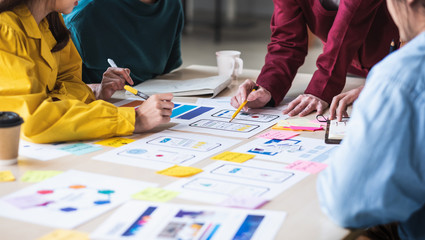 Close up ux developer and ui designer brainstorming about mobile app interface wireframe design on table with customer breif and color code at modern office.Creative digital development agency.