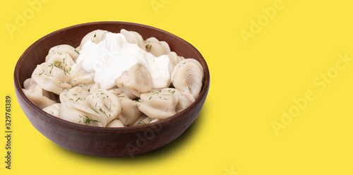 delicious dumplings with sour cream sprinkled with dill in a plate of red clay close up on a yellow background