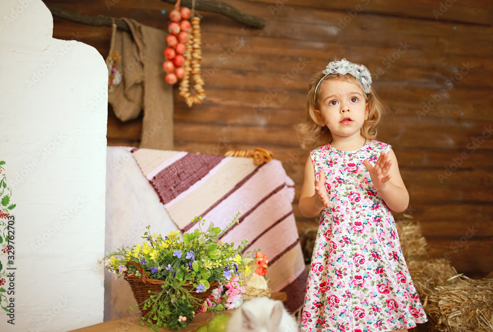 little girl stroking a white rabbit, a house with Easter eggs and hay