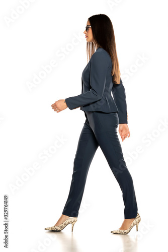 Side view of young beautiful business woman in a pants and jacket walking on white background