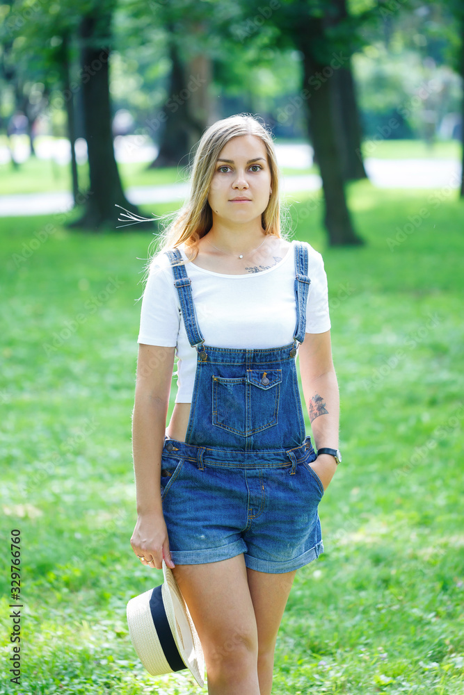 young beautiful girl in denim overalls and a light hat walking in the park young beautiful girl in denim overalls and a light hat walking in the park