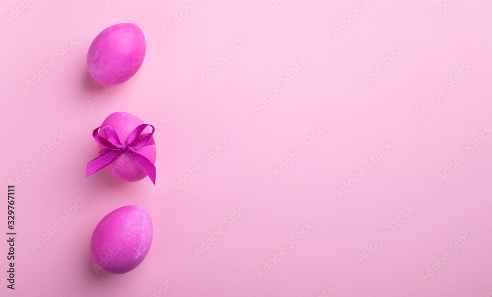 Bright pink eggs with satin bow on a pink background. Festive spring concept. Color trend.