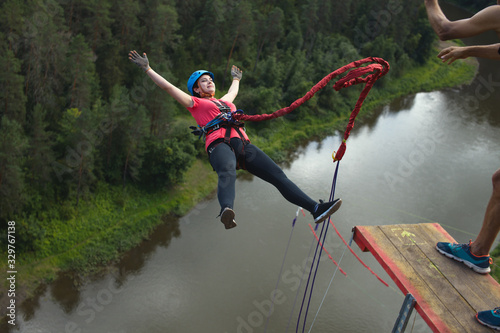 Young woman, tethered to a safety rope, falls from a great height into a deep canyon on the background of a river, close-up. Ropejumping. photo