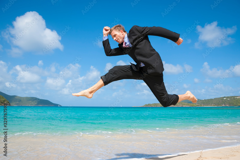Excited businessman jumping barefoot in his suit above an empty tropical beach Excited businessman jumping barefoot in his suit above an empty tropical beach