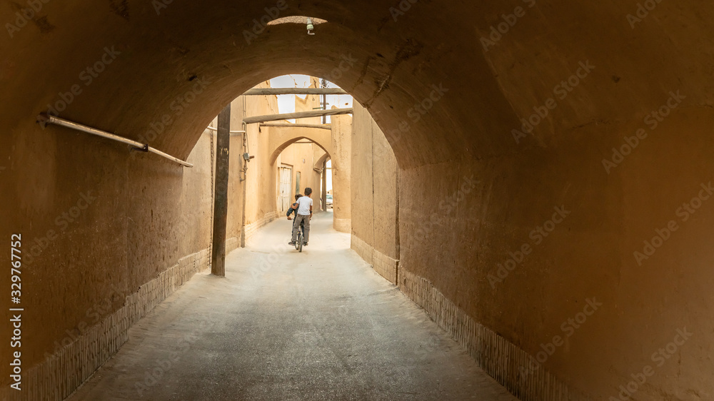 Kid on a bicycle riding in the narrow street of old city Yazd, Iran.