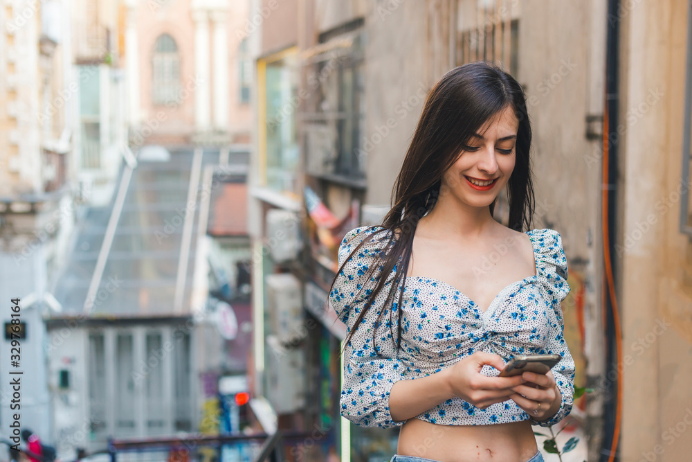 Cheerful brunette woman looking to her mobile phone and smiling in a street copy space