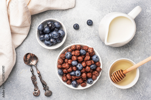 Chocolate flakes made from natural cereals with fresh blueberries, honey and milk. The concept of a healthy wholesome Breakfast. Grey concrete background