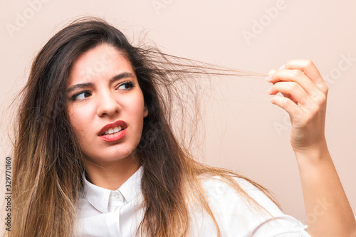 hair problems. young woman in white shirt checking her britle, damaged, and split hairs against pink background photo