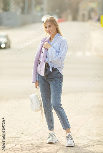 Outdoor fashion street stile portrait of pretty woman in casual outfit walking in city. Beautiful blonde girl or student enjoying weekends.