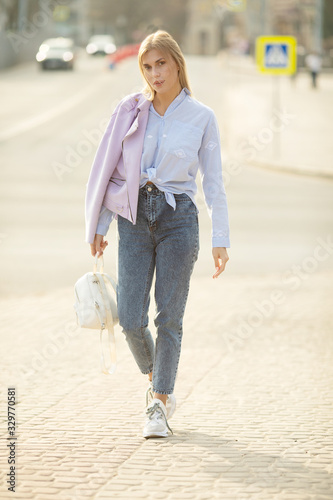 Outdoor fashion street stile portrait of pretty woman in casual outfit walking in city. Beautiful blonde girl or student enjoying weekends.