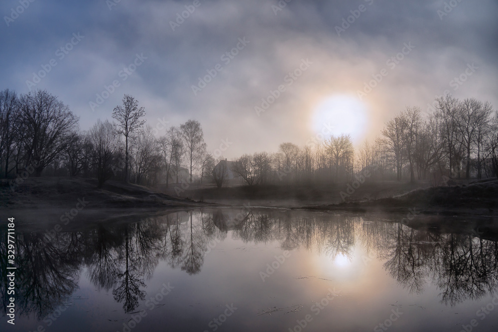 Early morning, fog glade, grass and trees in hoarfrost and a lake house.