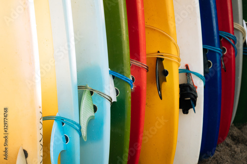 Close up Set of different color surf boards with fins in a stack on sandy beach for rent. Multicolored surfboards as rainbow.
