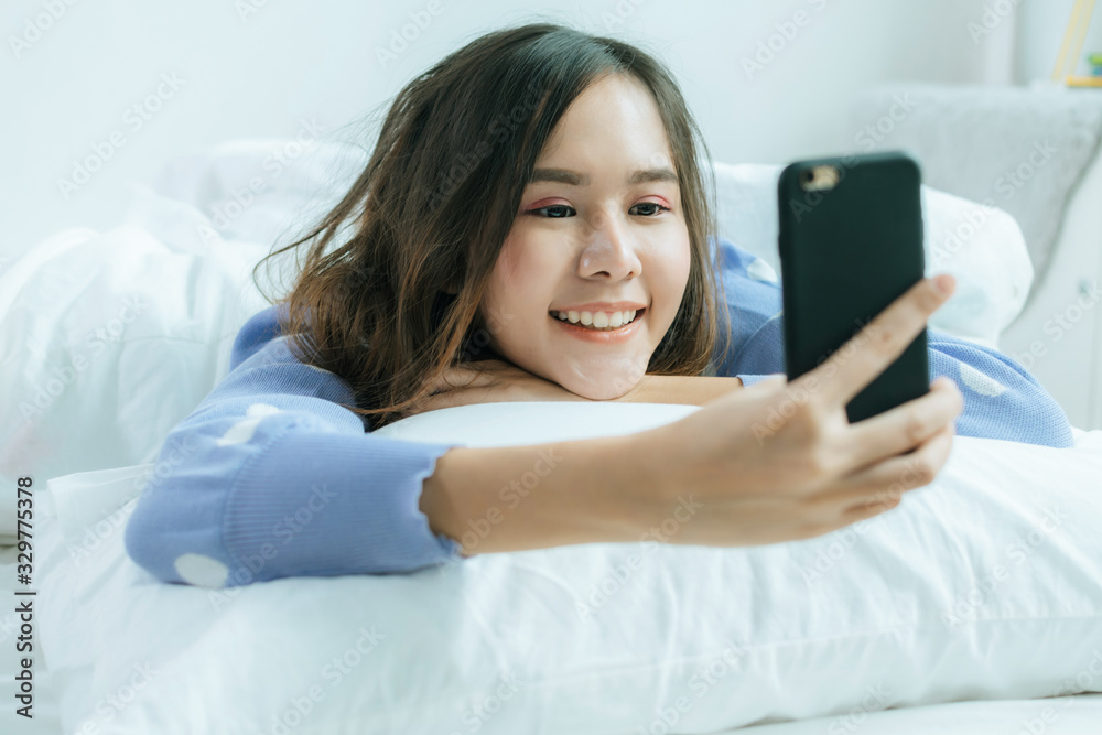 happy asian pretty woman in casual clothing smiling take selfie and video call on mobile phone and lying with pillow on bed in bedroom at home, lifestyle, internet technology, social network concept happy asian pretty woman in casual clothing smiling take selfie and video call on mobile phone and lying with pillow on bed in bedroom at home, lifestyle, internet technology, social network concept