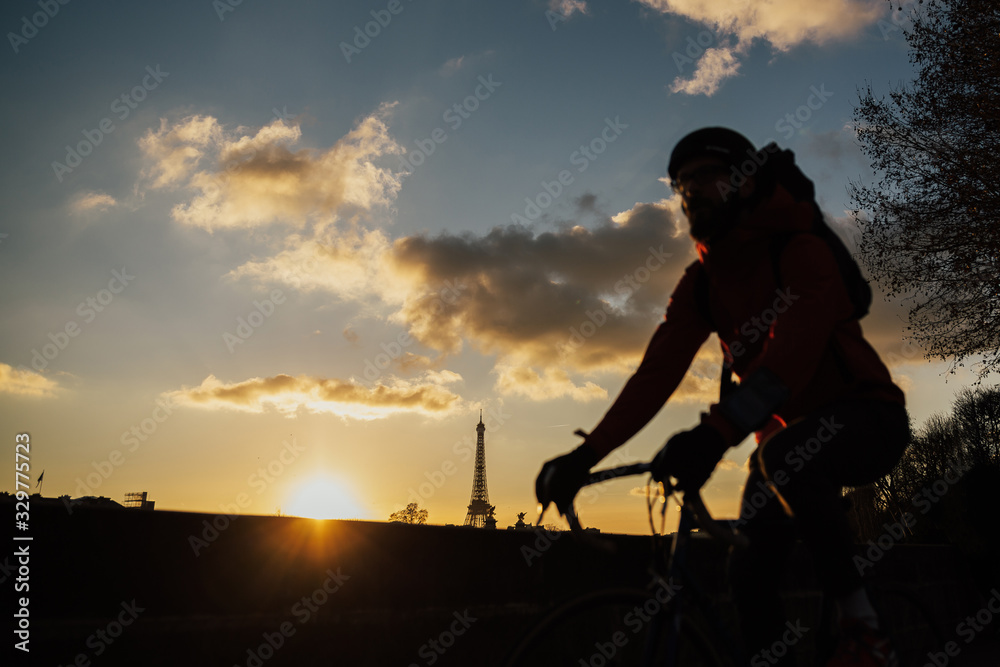 Man cycling through Parisian streets in sunset - abstract motion blur shot. Man on a bike riding with Eiffel tower on background. 