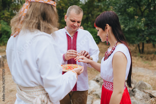 The wedding ceremony of the newlyweds in embroidered clothes  in the old Ukrainian traditions of paganism. Ethnic rite for newlyweds in Ukraine. The bride and groom put on gold rings to each other.