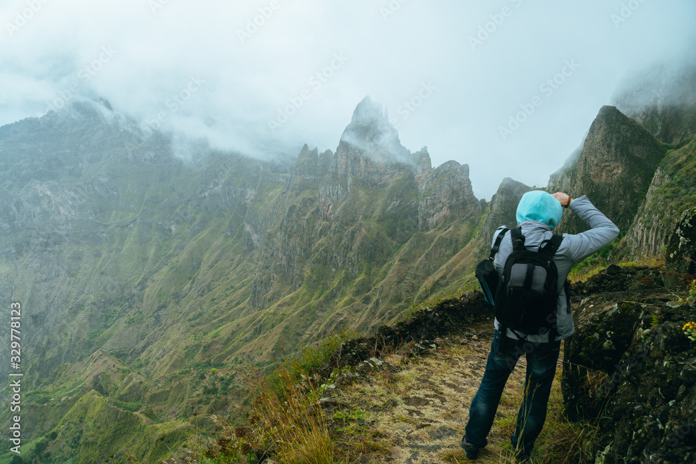 Hiker with camera in the steep mountainous terrain shooting a foto of lush canyon valley on the path from Xo-Xo Valley. Santo Antao Island, Cape Verde Hiker with camera in the steep mountainous terrain shooting a foto of lush canyon valley on the path from Xo-Xo Valley. Santo Antao Island, Cape Verde
