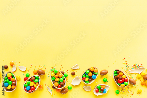 Chocolate Easter eggs and colorful candies on yellow paper background. flat lay, copy space, top view, overhead, template, mockup
