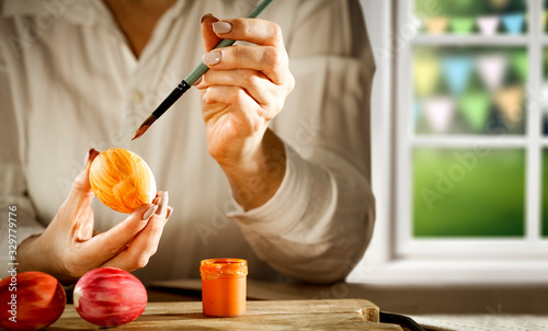 Woman hands painting easter eggs with brush.Free space for your product on kitchen board.White window in home interior and blurred landscape of park with spring girlands.Sunny warm day,sun light. photo