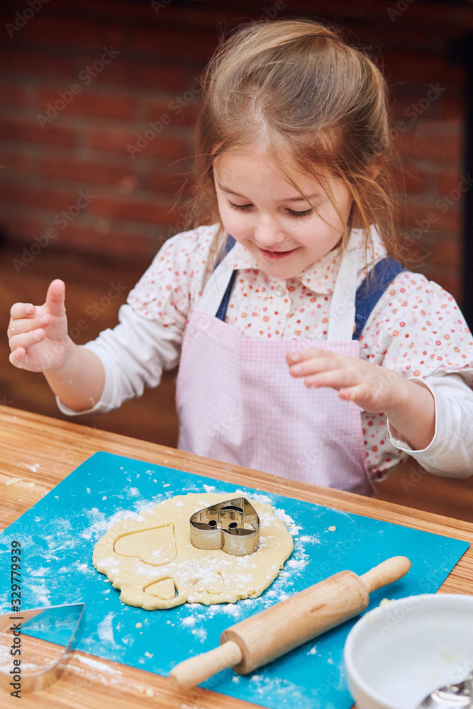 Little girl cutting the dough to heart shapes cookies. Kid taking part in baking workshop. Baking classes for children, aspiring little chefs. Learning to cook. Combining and stirring ingredients Little girl cutting the dough to heart shapes cookies. Kid taking part in baking workshop. Baking classes for children, aspiring little chefs. Learning to cook. Combining and stirring ingredients