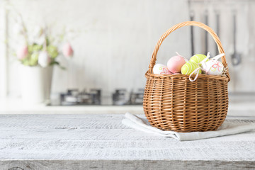 Wicker basket with easter colorful eggs on kitchen wooden table. Spring easter composition. Space for text.