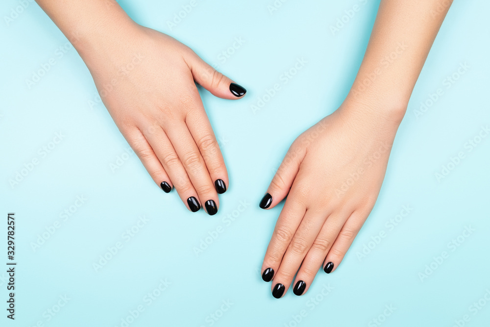 Womans hands with black manicure on silver circle and pastel blue background. Top view. - obrazy, fototapety, plakaty 