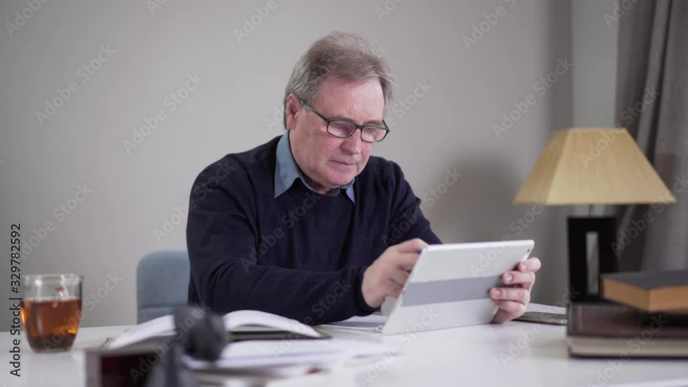 Senior Caucasian businessman scrolling tablet screen and shaking head. Portrait of mature man surfing Internet indoors. Lifestyle, activity, business, overworking. Senior Caucasian businessman scrolling tablet screen and shaking head. Portrait of mature man surfing Internet indoors. Lifestyle, activity, business, overworking.