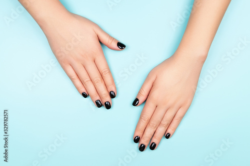 Womans hands with black manicure on silver circle and pastel blue background. Top view.