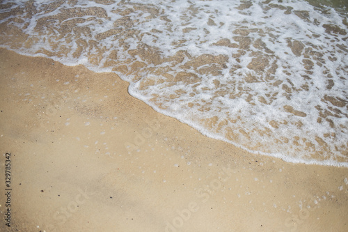 Beautiful natural photo background with empty copyspace. White foamy sea wave splashing at sandy beach peacefully.