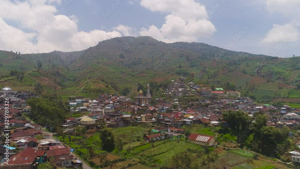 asian town with mosque in mountains among agricultural land, rice terraces. mountains with farmlands, rice fields, village, fields with crops, trees. Aerial view farm lands on mountainside. tropical asian town with mosque in mountains among agricultural land, rice terraces. mountains with farmlands, rice fields, village, fields with crops, trees. Aerial view farm lands on mountainside. tropical