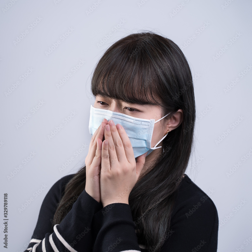 Woman coughing with mask - young Asian covering the mouth, feeling unwell with wearing medical blue face mask isolated on white background, close up. Woman coughing with mask - young Asian covering the mouth, feeling unwell with wearing medical blue face mask isolated on white background, close up.