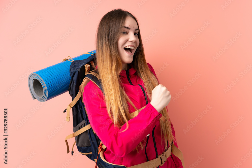 Obraz premium Young mountaineer girl with a big backpack isolated on pink background celebrating a victory