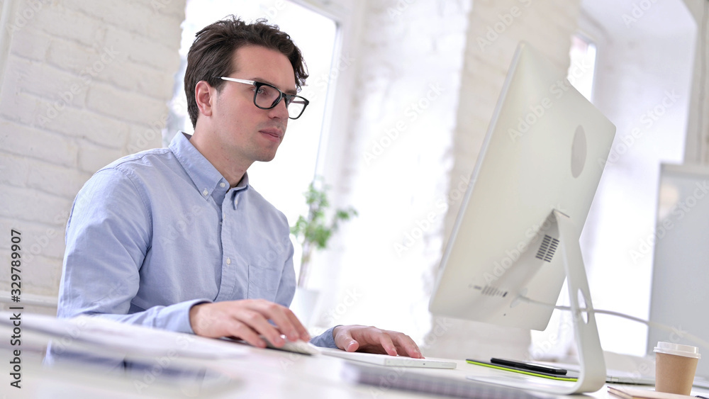 Fototapeta premium Working Young Man Reading Documents and using Laptop in Office