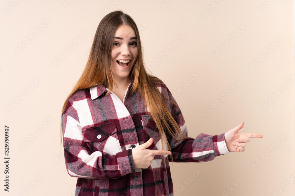 Young caucasian woman isolated on beige background surprised and pointing side Young caucasian woman isolated on beige background surprised and pointing side