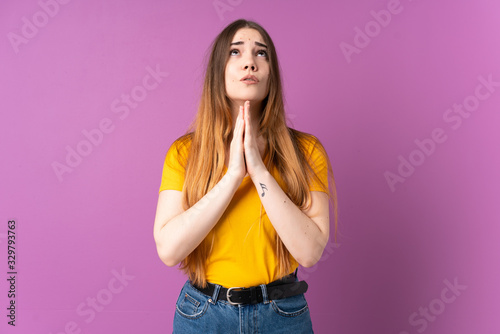 Young caucasian woman isolated on purple background keeps palm together. Person asks for something