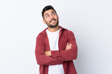 Young handsome man with beard wearing a corduroy jacket over isolated white background looking up while smiling