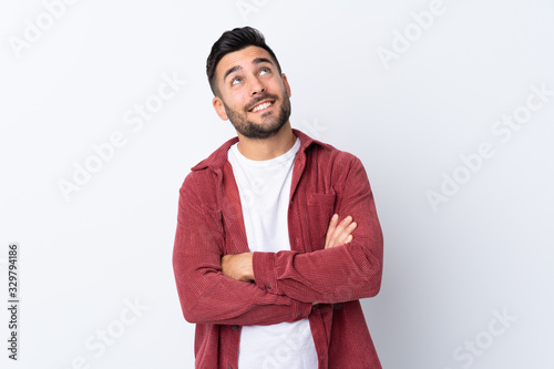 Young handsome man with beard wearing a corduroy jacket over isolated white background looking up while smiling photo