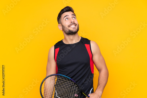 Tennis player man over isolated yellow wall looking up while smiling © luismolinero
