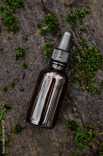 Bottle of serum on dark background from moss