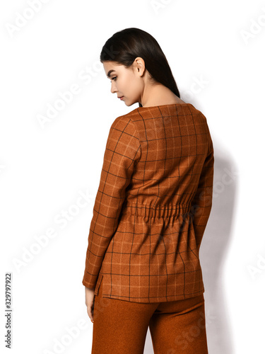 Young brunette woman in stylish business suit trousers and jacket is standing back to us over white background photo