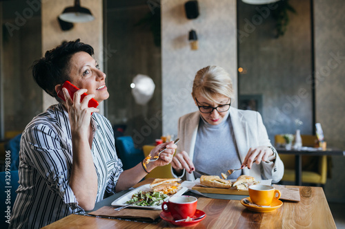 women friends having lunch break in restaurant, using mobile phone