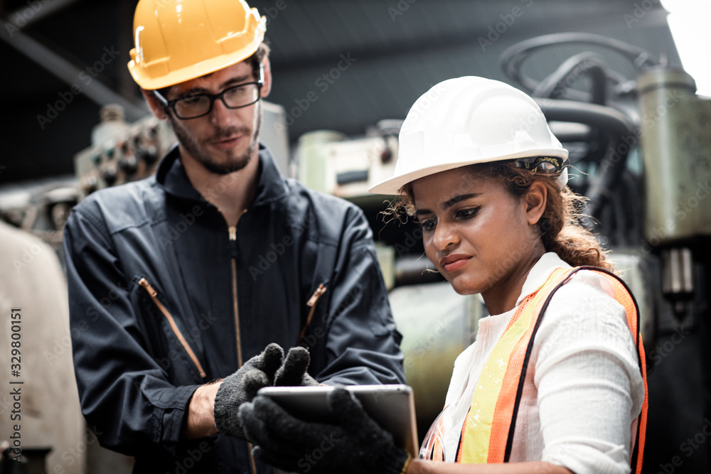 Two maintenance engineers discuss inspect relay checking information and protection system on a tablet computer in a factory. They work a heavy industry manufacturing factory. Two maintenance engineers discuss inspect relay checking information and protection system on a tablet computer in a factory. They work a heavy industry manufacturing factory.