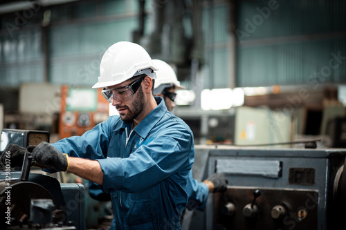 Canvas-taulu Men industrial engineer wearing a white helmet while standing in a heavy industrial factory behind