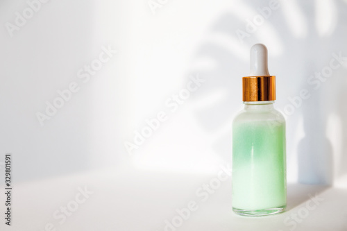 Natural cosmetics: serum with dropper and shadow from monstera leave on white background.