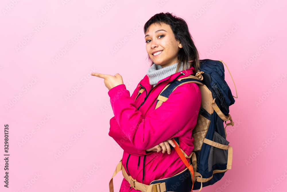 Young mountaineer girl with a big backpack over isolated pink background pointing finger to the side Young mountaineer girl with a big backpack over isolated pink background pointing finger to the side