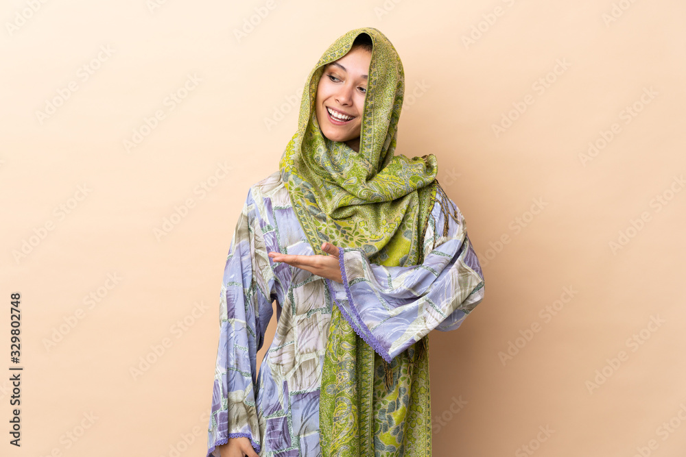 Indian woman isolated on beige background presenting an idea while looking smiling towards