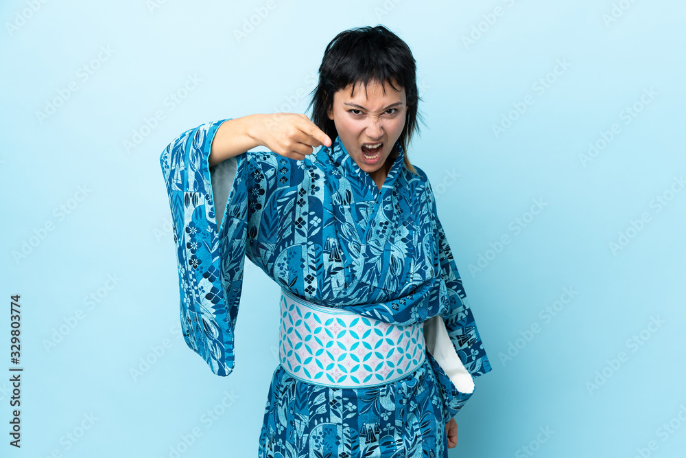 Young woman wearing kimono over isolated blue background frustrated and pointing to the front Young woman wearing kimono over isolated blue background frustrated and pointing to the front