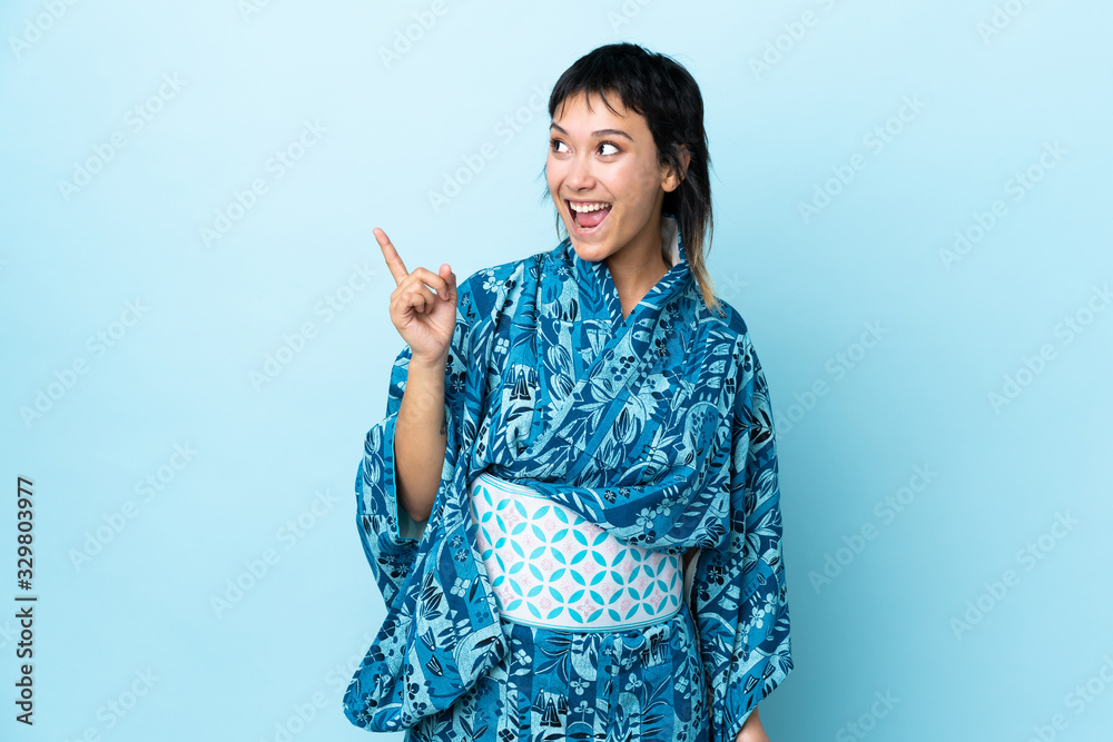 Young woman wearing kimono over isolated blue background intending to realizes the solution while lifting a finger up Young woman wearing kimono over isolated blue background intending to realizes the solution while lifting a finger up